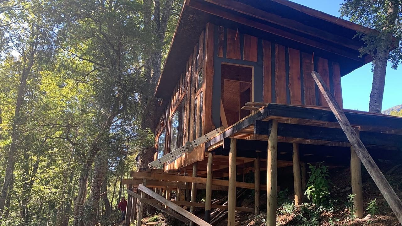 Cabaña de panel SIP construida sobre pilotes de madera en un terreno con pendiente